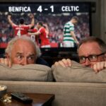 Dermot Desmond and Michael Nicholson (Celtic executive) with glasses hiding behind their couch whilst watching tv as the scre